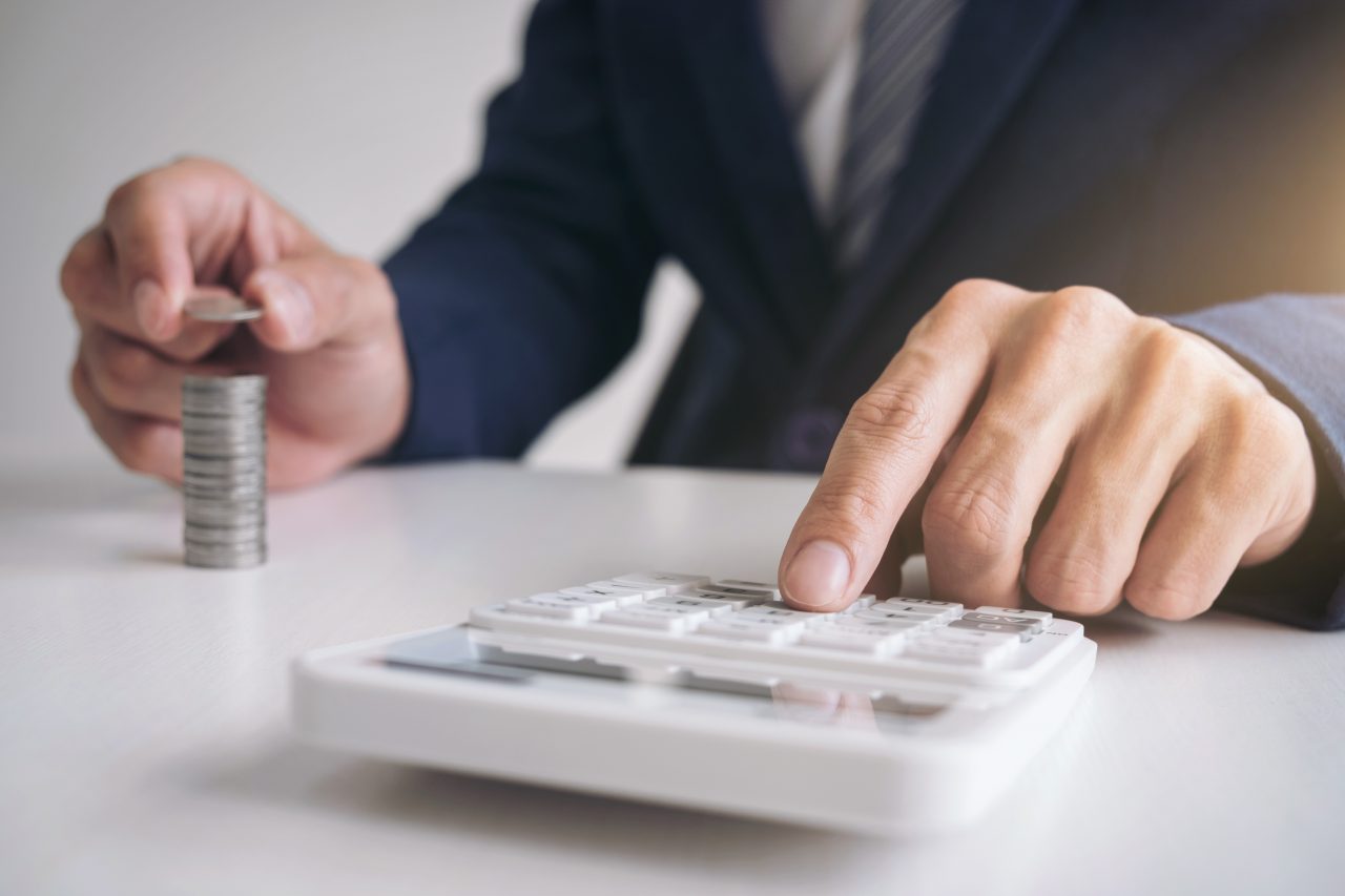 Image of person's hands using a calculator on a desk and counting coins off to the side.