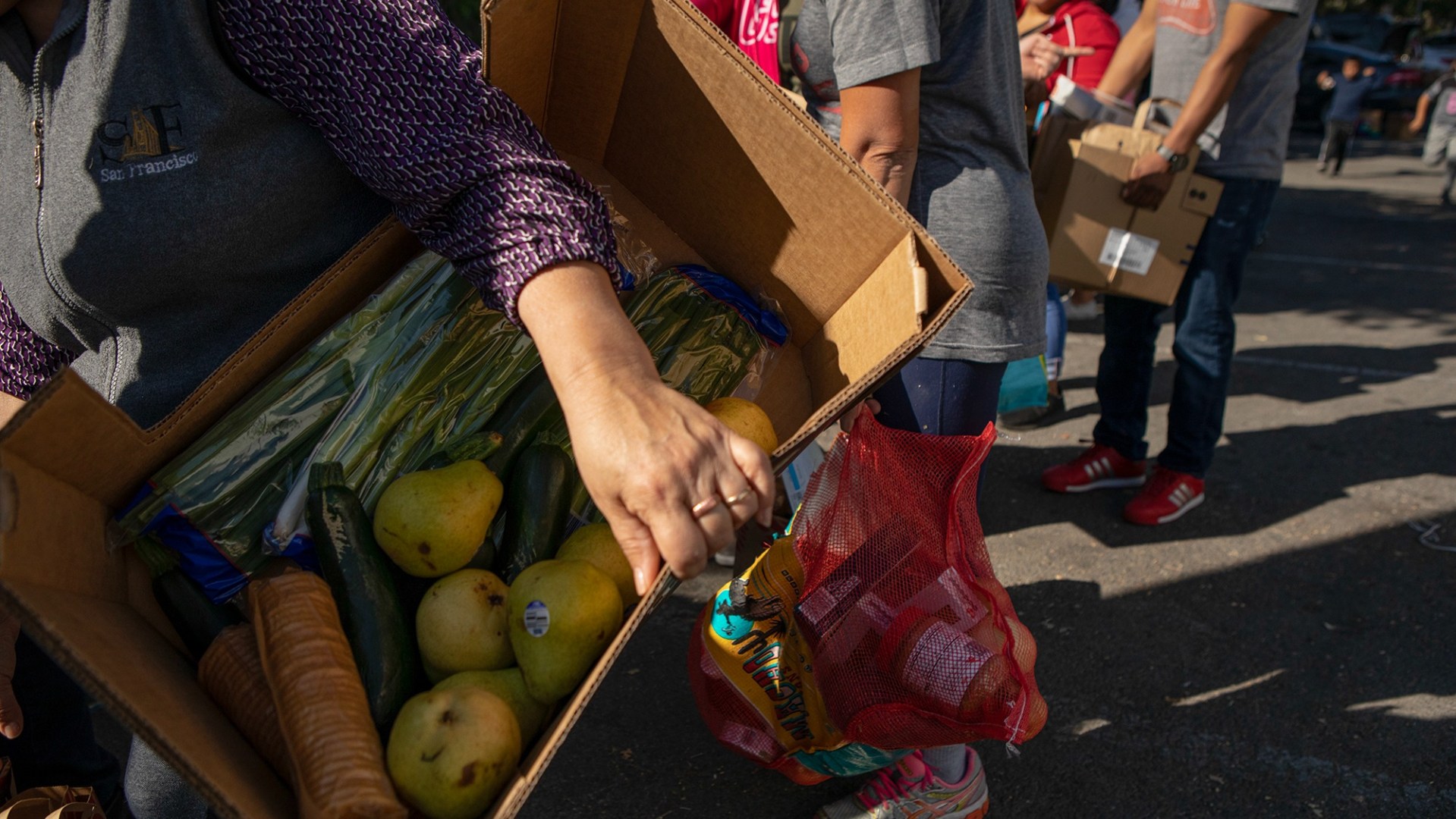 A hand holding a cardboard box with fresh produce